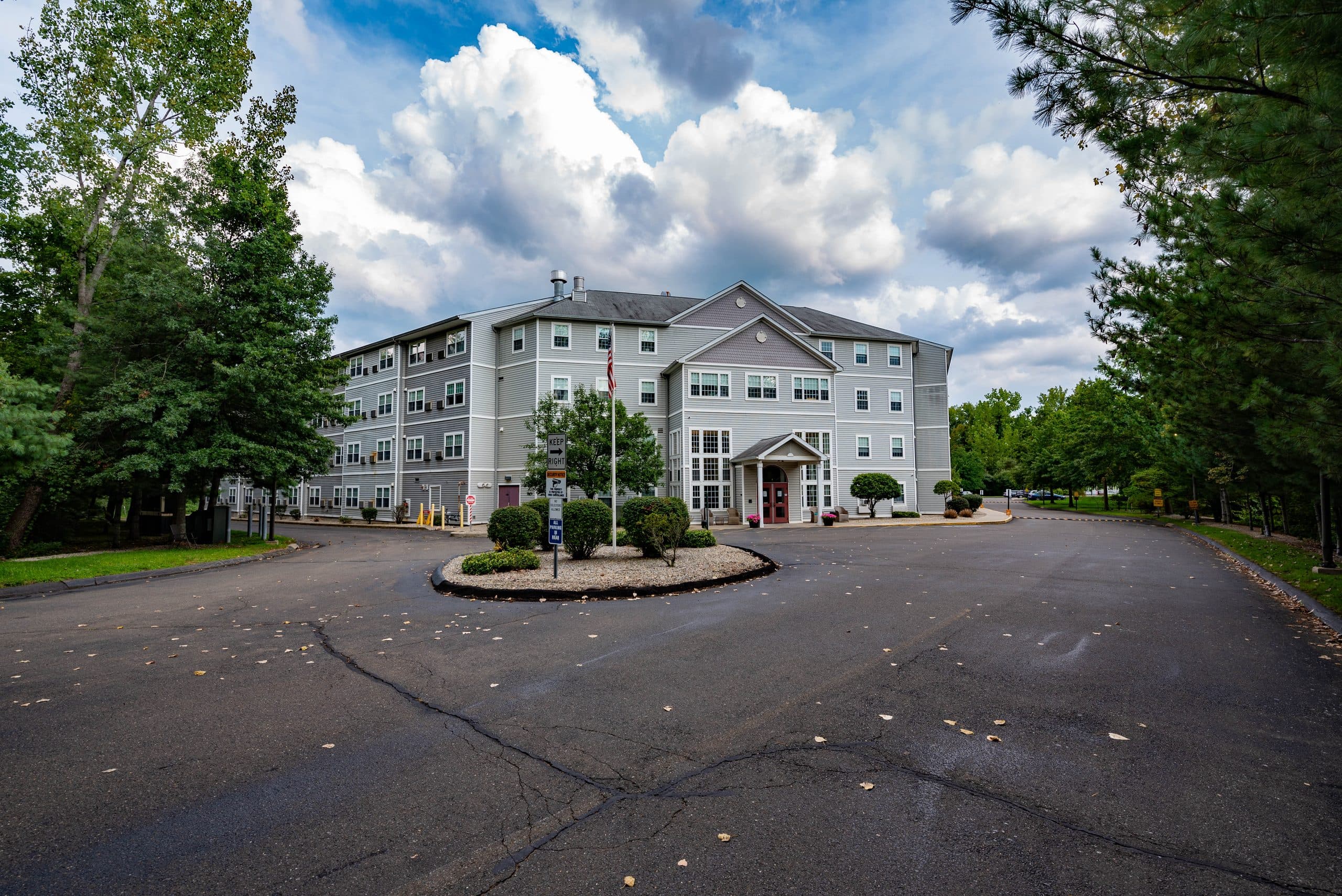 Carmen Romano Apartments — a four-storey clapboard building behind its circular drive and flagpole, framed by mature trees