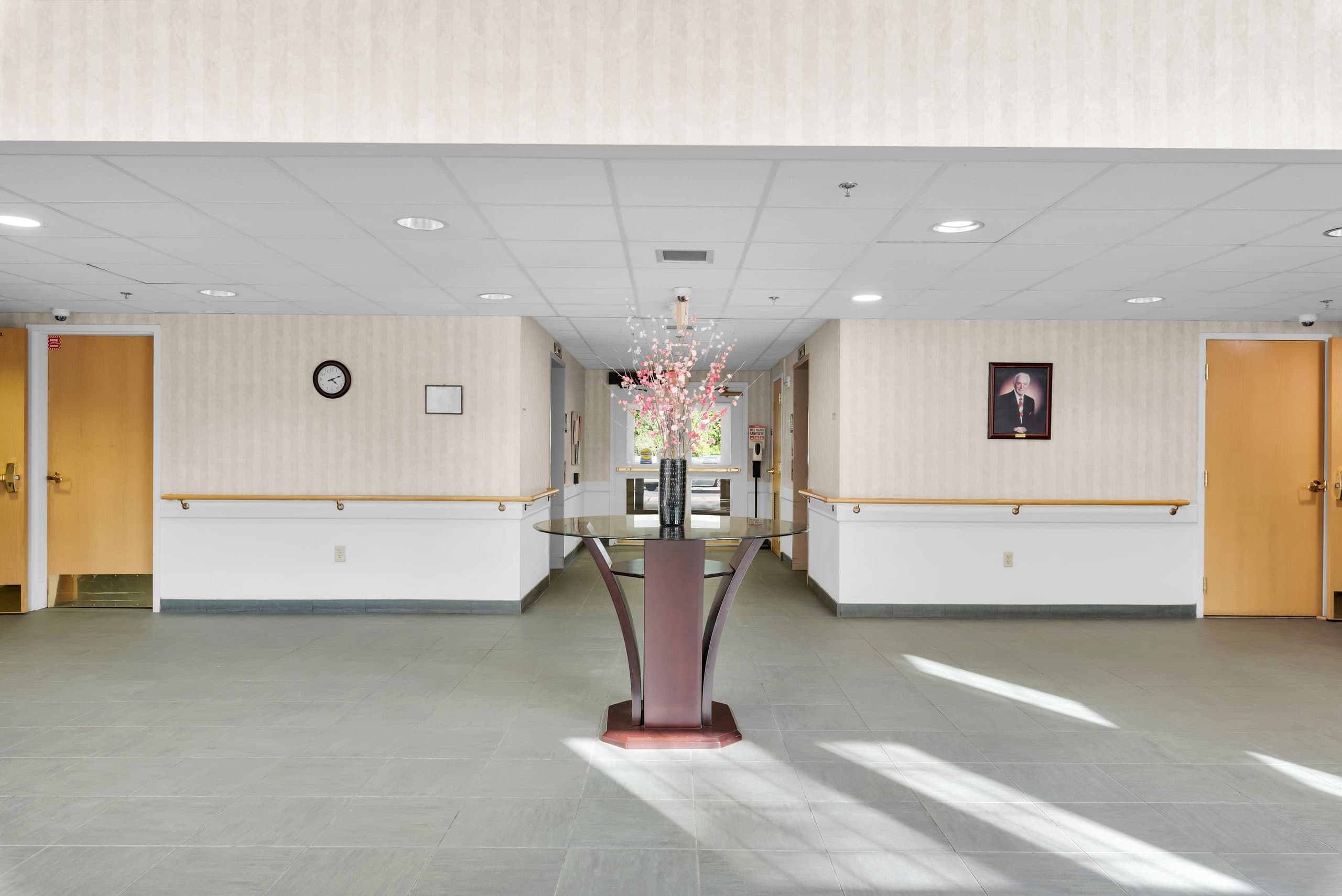 The Carmen Romano lobby — a bright, tiled entry with seating, fresh flowers on a pedestal table, and handrails along the walls
